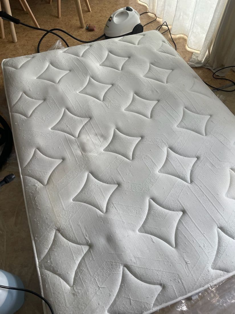 Matelas 2 places à motif matelassé pendant le nettoyage, avec le nettoyeur vapeur en arrière-plan